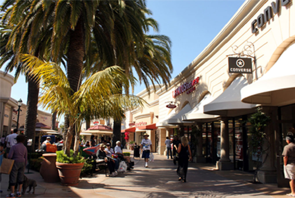 Several people sitting, standing, and walking in an open area outside shops in Carlsbad, CA