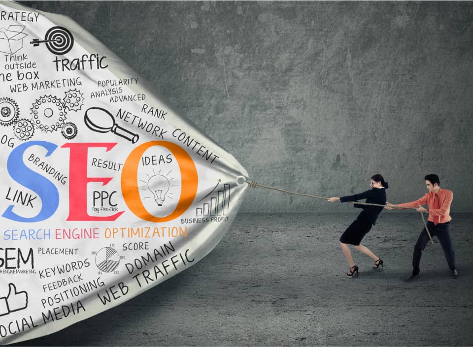 Two people pull on a large graphic labeled "SEO" surrounded by related terms and icons, illustrating the concept of search engine optimization.