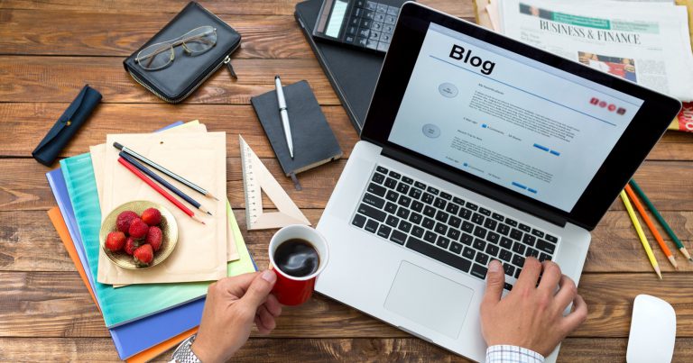 Person working on a blog on his laptop while holding a cup of coffee