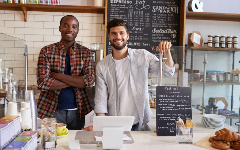 Two smiling men standing inside the counter of a coffee shop