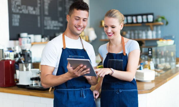 Male and female baristas wearing denim aprons and looking at a tablet