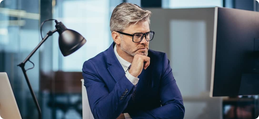 A gray-haired man with glasses thinks about the tasks
