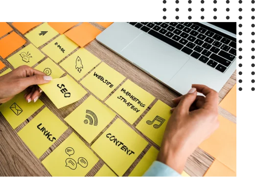 Person arranging yellow sticky notes labeled with terms like "SEO," "Links," "Content," and "Marketing Strategy" next to a laptop on a wooden desk.