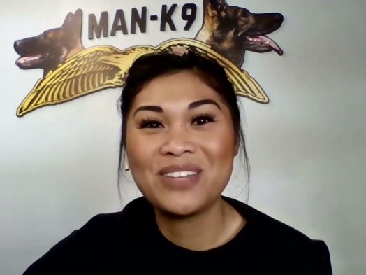 smiling woman with Man K-9 text with two face of dogs and an eagle logo on the wall